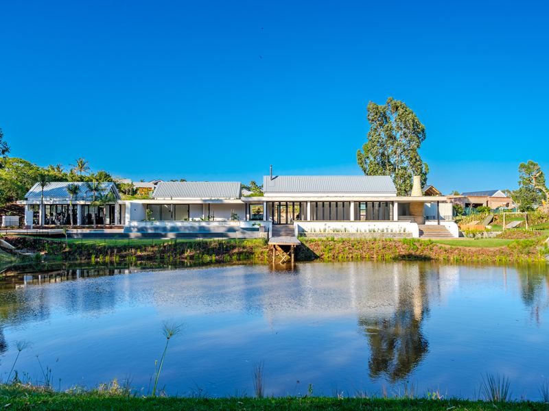 A stunning rear view of a modern residence featuring a metal roof, expansive glass doors, and a wooden deck overlooking a tranquil pond.