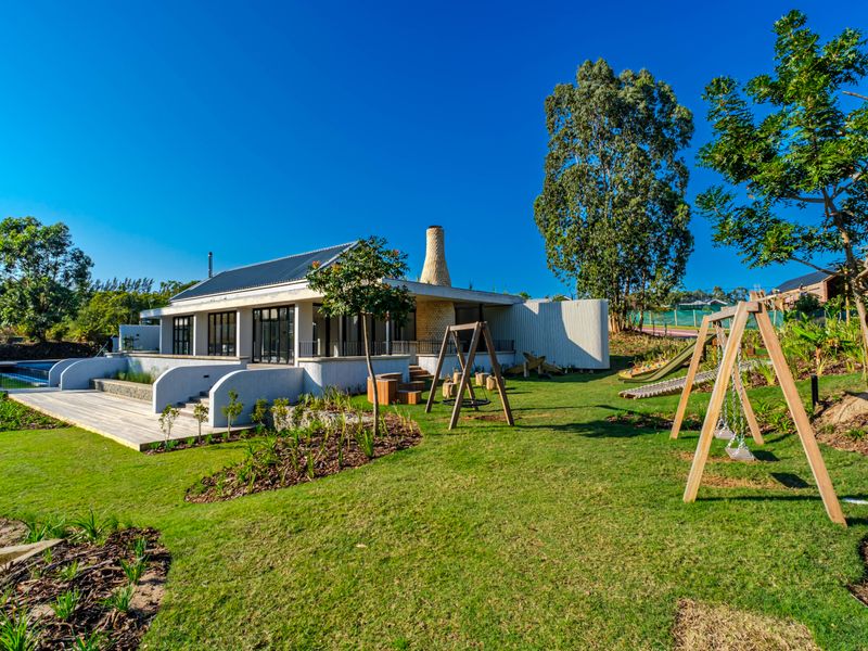 A beautifully landscaped rear garden featuring a spacious timber deck, modern architectural design with a prominent stone chimney, and large glass doors.