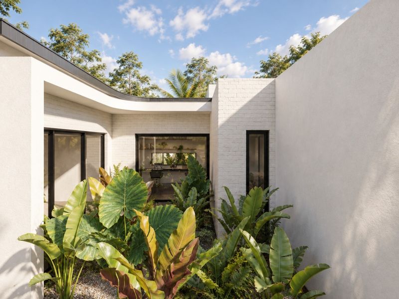 A modern, well-maintained rear courtyard featuring white painted brick walls, black aluminum-framed windows, and lush tropical landscaping.