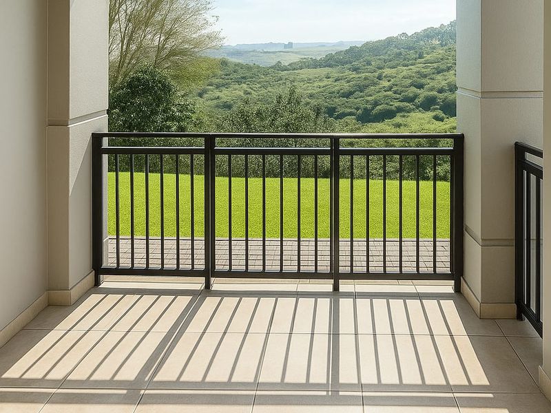 A spacious covered balcony featuring neutral floor tiles and a metal balustrade, offering scenic views of the surrounding landscape.