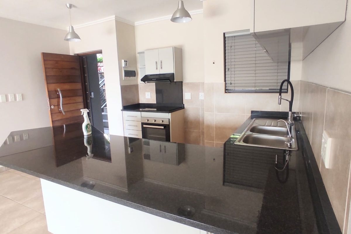 Modern kitchen featuring granite countertops, built-in oven, hob, extractor fan, and double bowl sink with contemporary finishes and ample cabinetry.