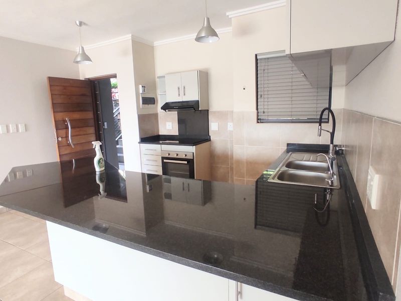 Modern kitchen featuring granite countertops, built-in oven, hob, extractor fan, and double bowl sink with contemporary finishes and ample cabinetry.