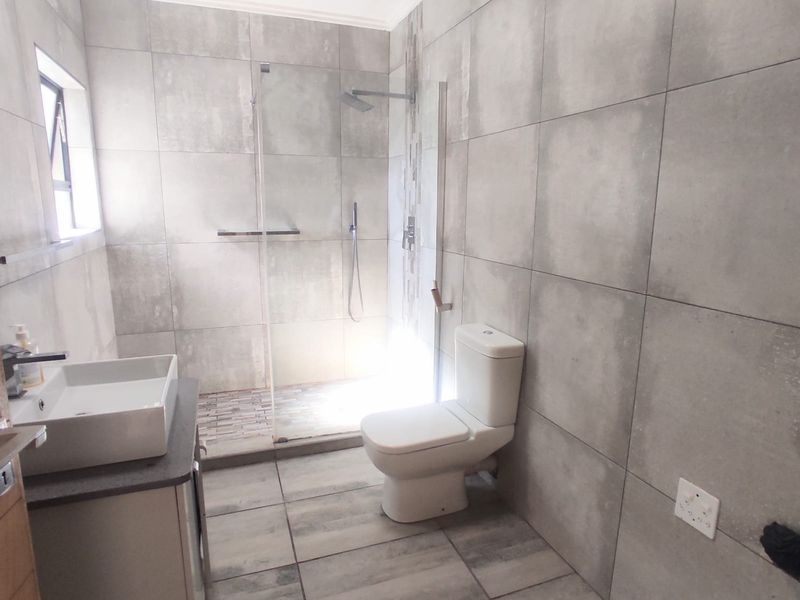 Modern bathroom featuring large format grey tiling, a walk-in shower with glass screen, a vanity basin, and a toilet.