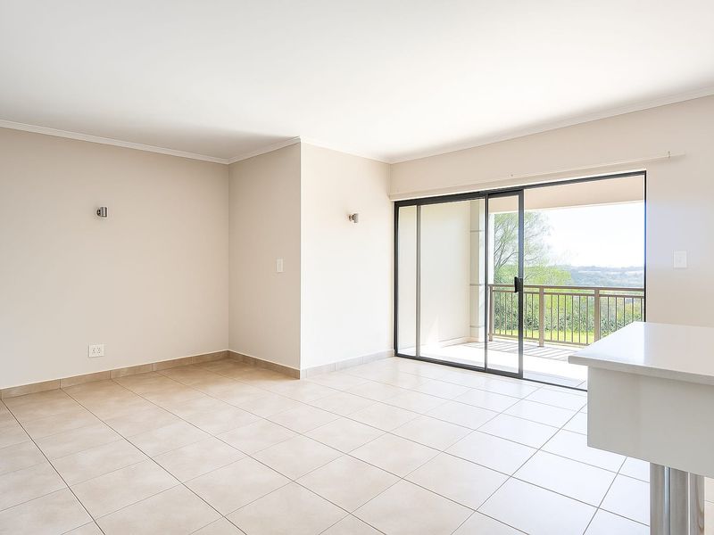Bright and spacious open-plan living area featuring neutral tiled flooring, modern wall lighting, and seamless access to a private balcony with scenic views.