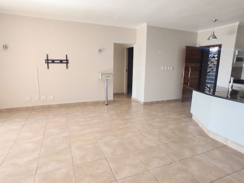 Spacious open-plan living area featuring neutral tiled flooring, a kitchen island with breakfast counter, and direct access to the main entrance.