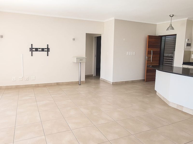 Spacious open-plan living area featuring neutral tiled flooring, a breakfast bar with granite countertop, and direct access to the entrance.
