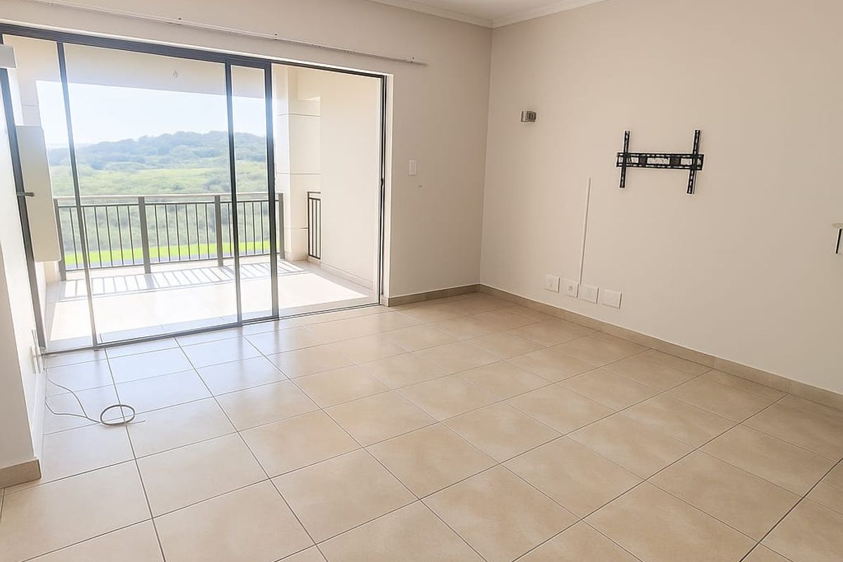 Spacious, empty living area featuring neutral tiled flooring, a wall-mounted TV bracket, and large sliding glass doors opening onto a balcony with scenic views.