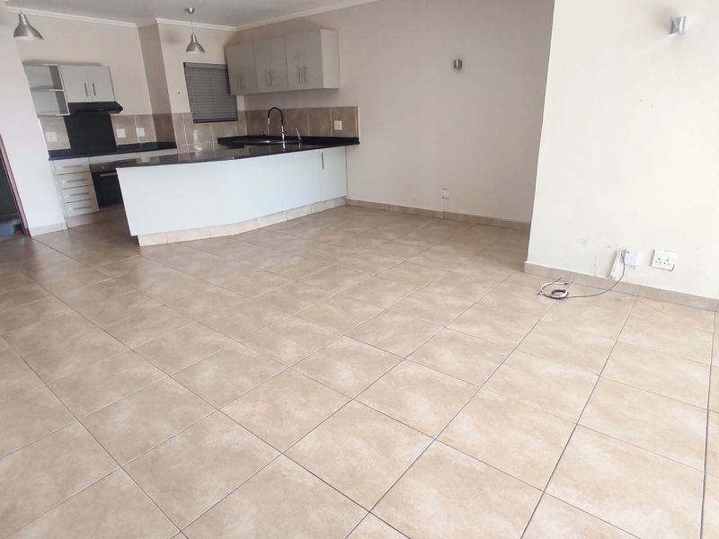 An open-plan living and kitchen area featuring tiled flooring, built-in cabinetry, and a functional kitchen layout in a vacant apartment setting.