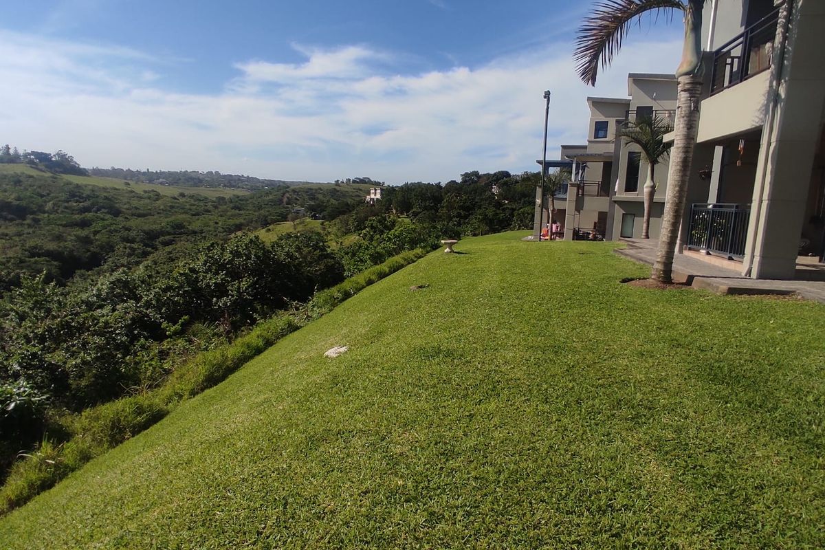 A spacious rear lawn area overlooking a scenic valley, featuring a well-maintained garden and access to the apartment's balcony.