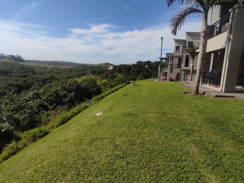 A spacious rear lawn area overlooking a scenic valley, featuring a well-maintained garden and access to the apartment's balcony.