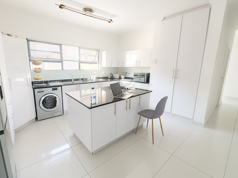 Modern kitchen featuring white cabinetry, a central island with stone countertops, tiled flooring, and integrated laundry facilities.