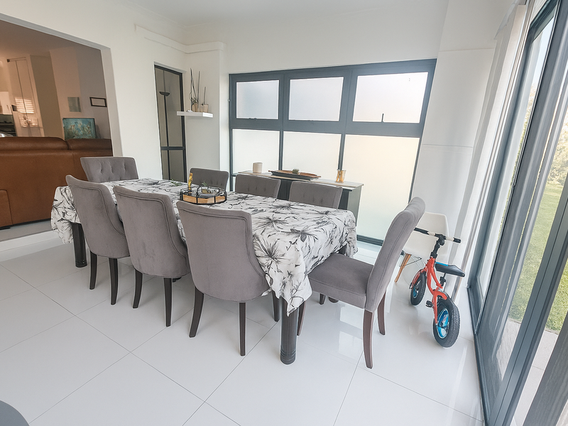 Bright and spacious dining area featuring large sliding glass doors, modern tiled flooring, and ample natural light, seamlessly connecting to the adjacent living space.