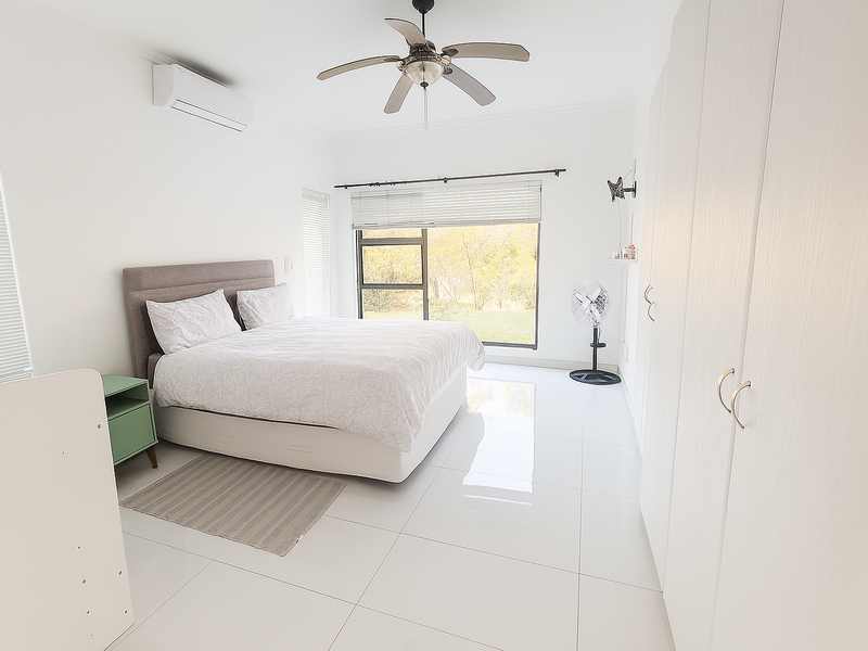 Bright and spacious bedroom featuring large windows, built-in cupboards, tiled flooring, a ceiling fan, and an air conditioning unit.