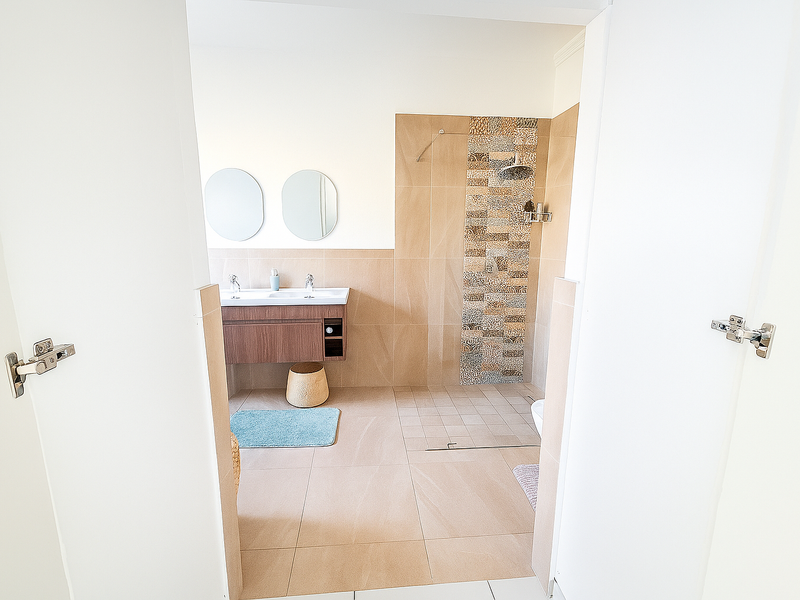 Modern bathroom featuring a double vanity with wall-mounted cabinetry and a spacious walk-in shower with decorative tiled accents.