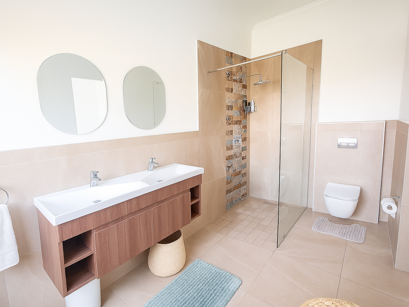 Modern bathroom featuring a double vanity, wall-mounted toilet, and a spacious walk-in shower with a rain shower head and decorative tiled accent wall.