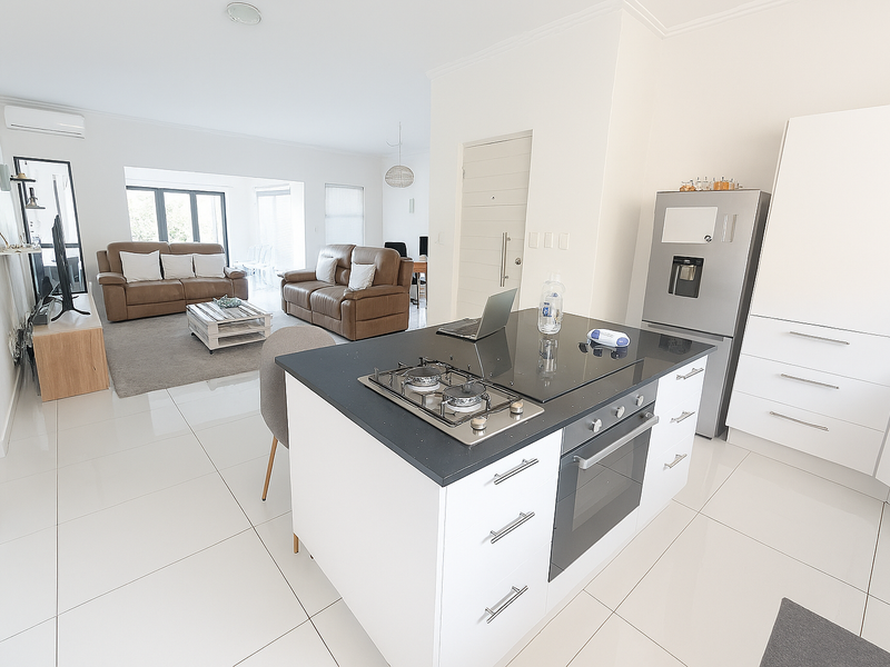 Modern open-plan living area featuring a sleek kitchen island with gas hob, built-in oven, and bright tiled flooring throughout the connected living space.