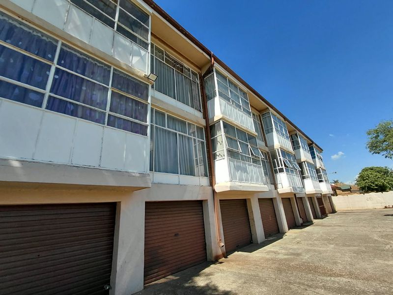 Exterior view of an apartment complex featuring a row of ground-level roller garage doors and upper-level enclosed balconies.