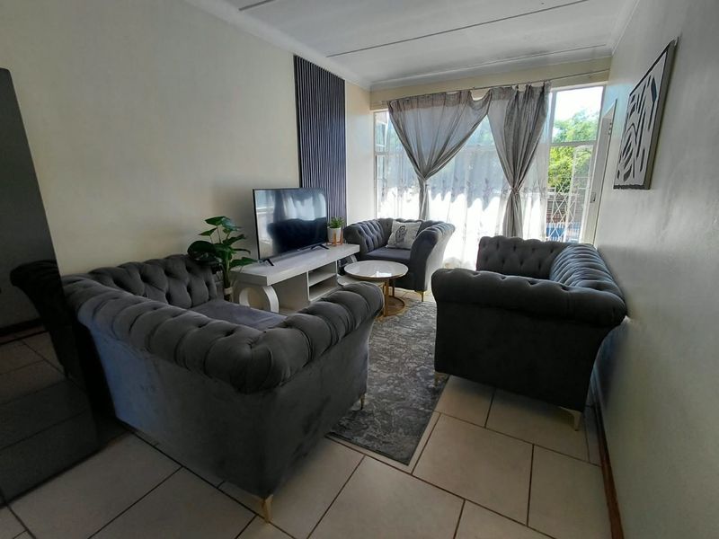 A comfortable living room featuring tiled flooring and a decorative accent wall panel, providing a functional space with natural light from the large window.