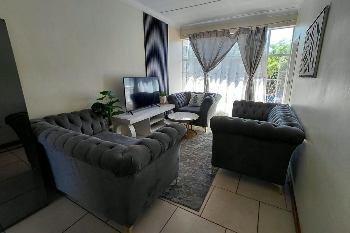 A comfortable living room featuring tiled flooring and a decorative accent wall panel, providing a functional space with natural light from the large window.