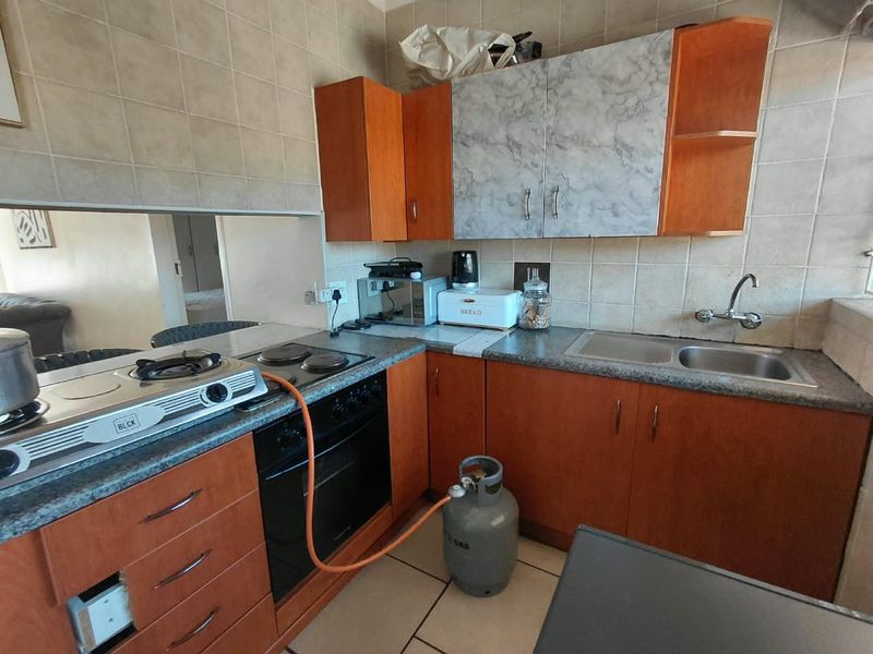 A dated kitchen featuring wood-tone cabinetry, laminate countertops, a stainless steel sink, and tiled backsplash, requiring modernization to improve functionality and aesthetic appeal.