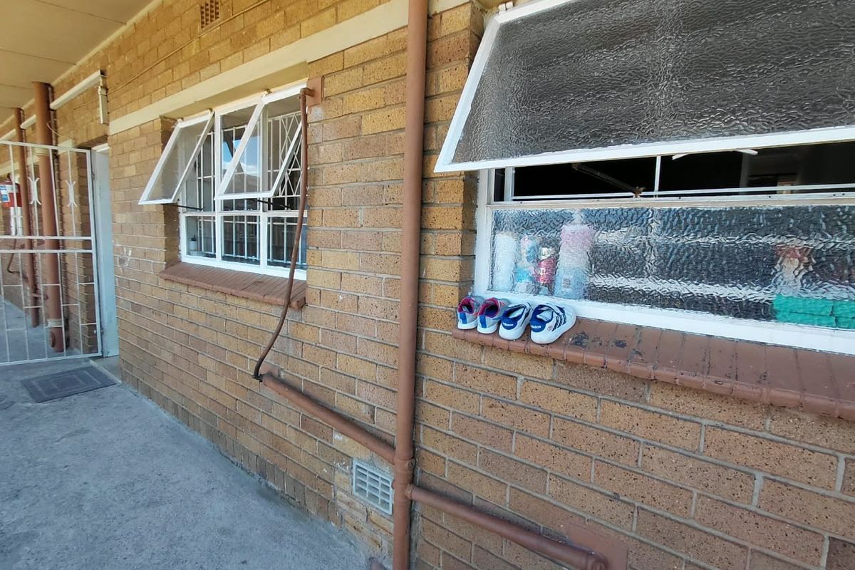 Exterior view of an apartment building featuring face brick walls, top-hung windows with security bars, and external plumbing infrastructure.