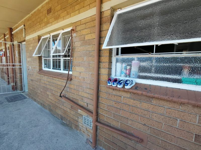 Exterior view of an apartment building featuring face brick walls, top-hung windows with security bars, and external plumbing infrastructure.