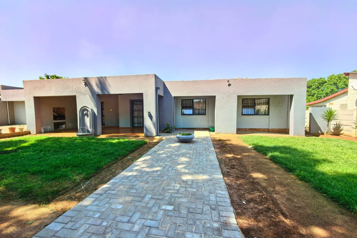 Rear view of the property featuring a paved walkway leading to a covered patio with a built-in braai and water feature.