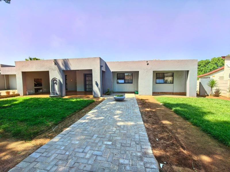 Rear view of the property featuring a paved walkway leading to a covered patio with a built-in braai and water feature.