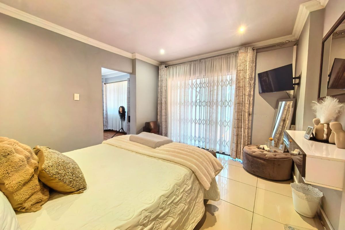 A well-lit bedroom featuring tiled flooring, crown molding, and a sliding glass door with an integrated security gate leading to an outdoor area.