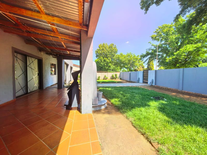 A covered patio with terracotta tiling overlooking a private garden and enclosed by a perimeter boundary wall.