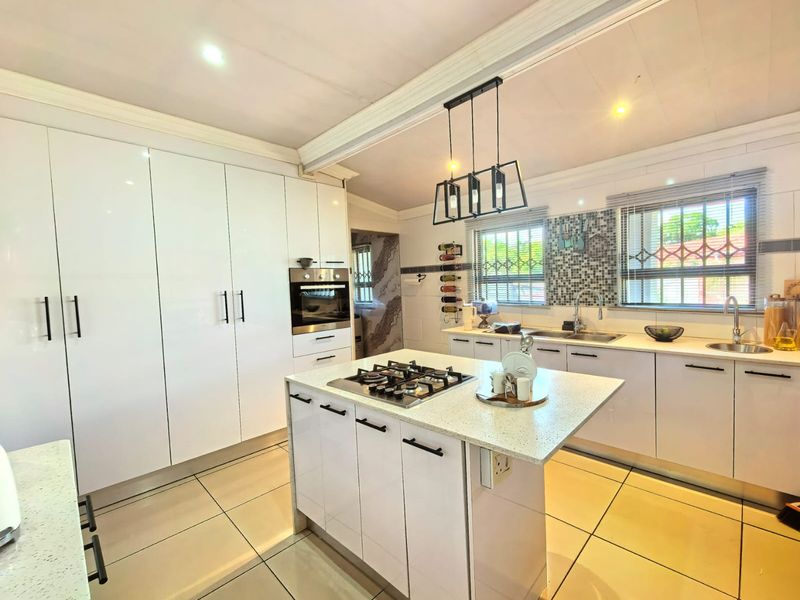 Modern kitchen featuring white cabinetry, a central island with a gas hob, quartz countertops, double sinks, and tiled flooring.