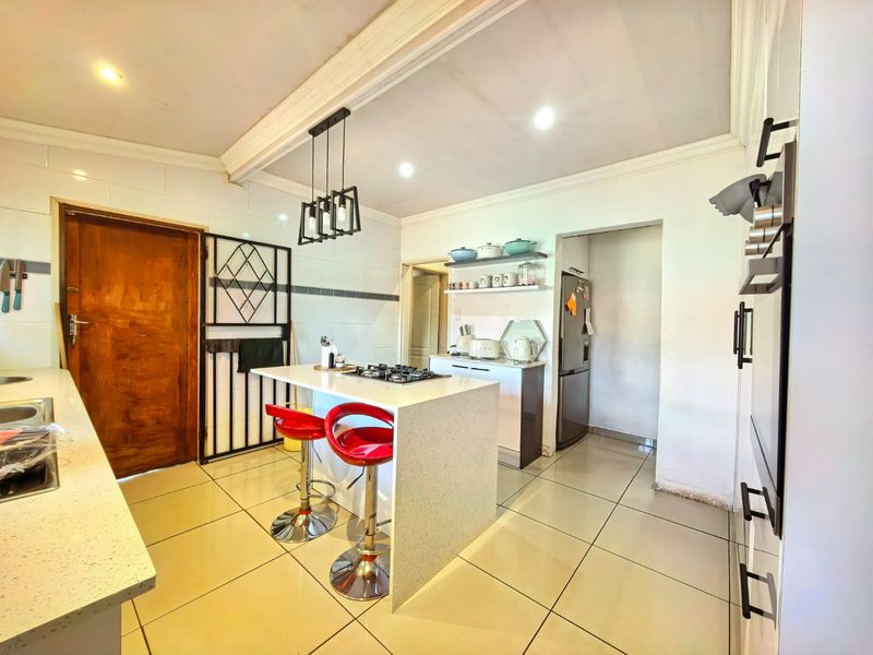 Modern kitchen featuring a central island with a built-in gas hob, tiled flooring, recessed lighting, and an adjacent scullery area.