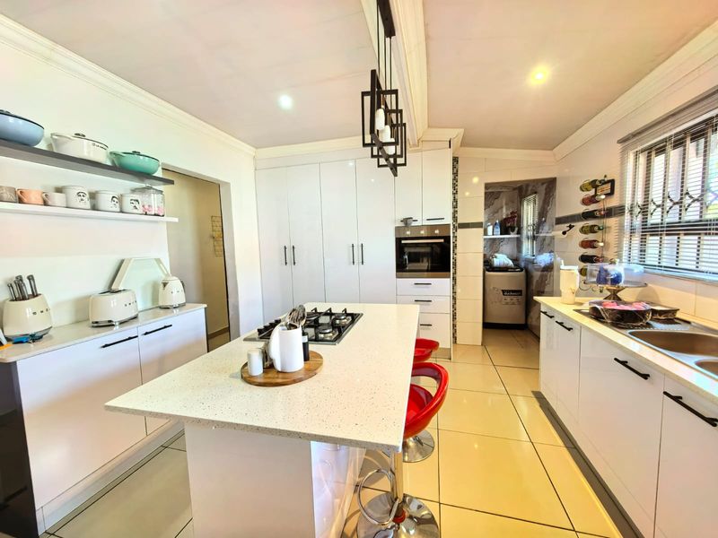 Modern kitchen featuring a central island with gas hob, high-gloss cabinetry, quartz countertops, and integrated oven, complemented by sleek pendant lighting and tiled floors.