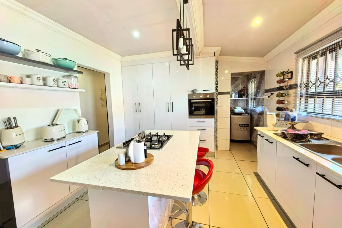 Modern kitchen featuring a central island with gas hob, high-gloss cabinetry, quartz countertops, and integrated oven, complemented by sleek pendant lighting and tiled floors.