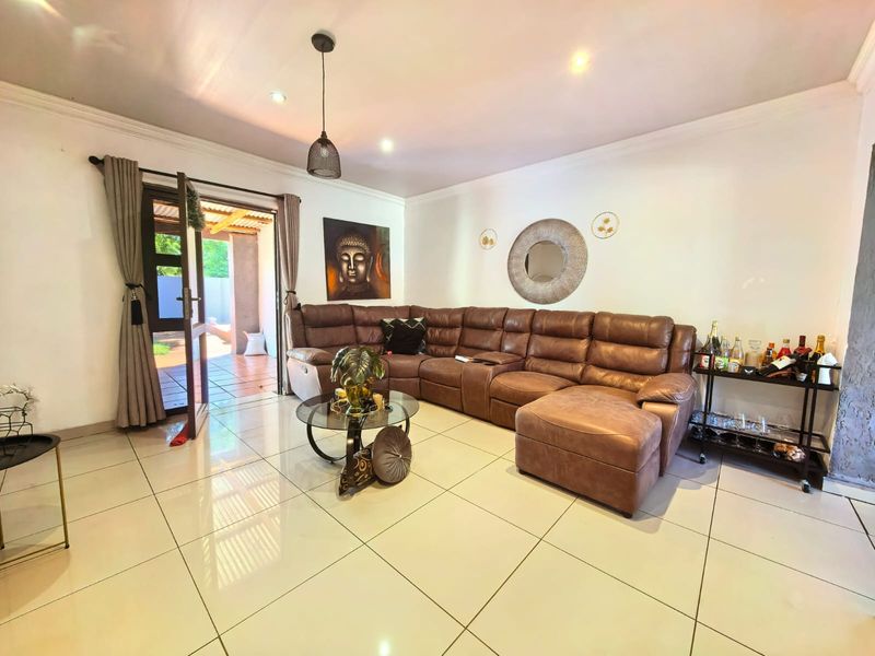 A bright and spacious living room featuring large format floor tiles, recessed lighting, and direct access to an outdoor patio area.