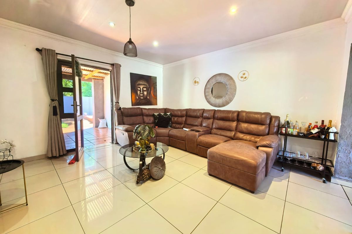 A bright and spacious living room featuring large format floor tiles, recessed lighting, and direct access to an outdoor patio area.