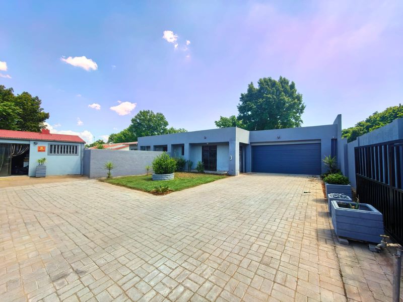 A well-maintained front exterior featuring a spacious paved driveway, a double garage, and a neat garden area with boundary walls.