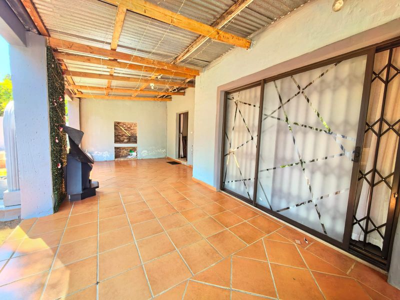 Covered patio area featuring tiled flooring, a built-in braai, and sliding glass doors with decorative security gates, offering a functional outdoor entertainment space.