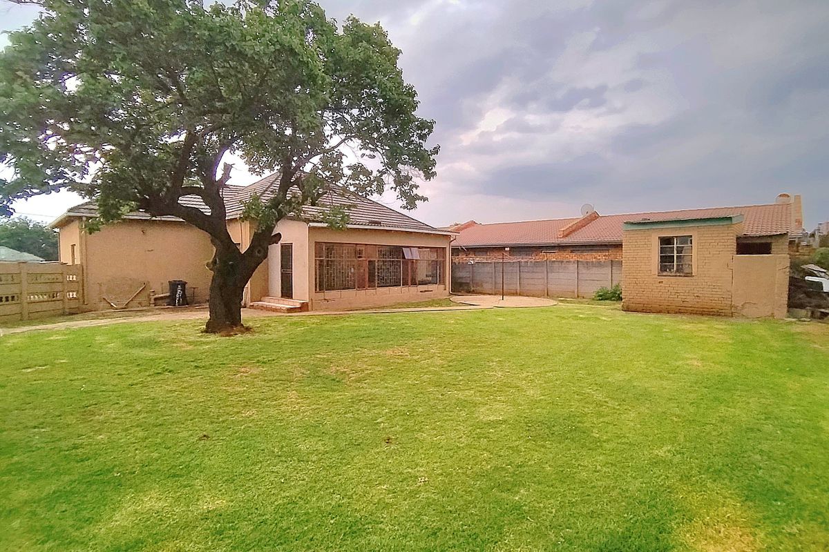 Spacious rear garden featuring a large lawn, mature tree, enclosed patio area, and a detached outbuilding with a tiled roof.