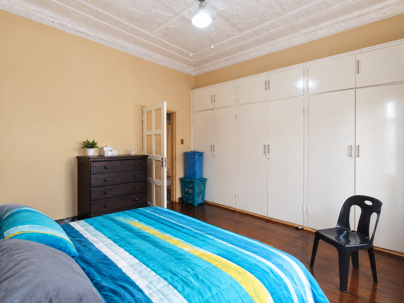 Spacious bedroom featuring extensive built-in cupboards, polished hardwood flooring, and an ornate ceiling with decorative cornicing.