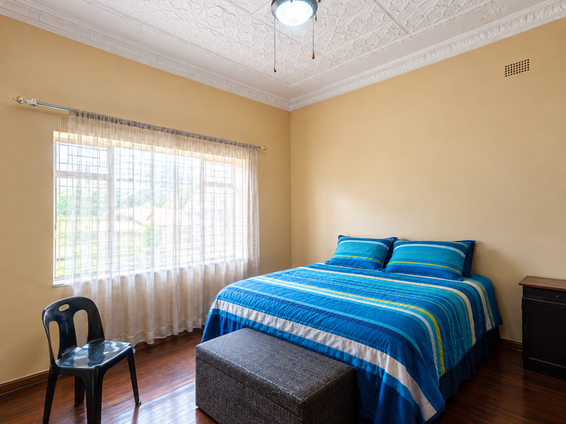 A well-lit bedroom featuring classic pressed metal ceilings, decorative cornicing, and polished hardwood flooring, offering a comfortable and character-filled living space.
