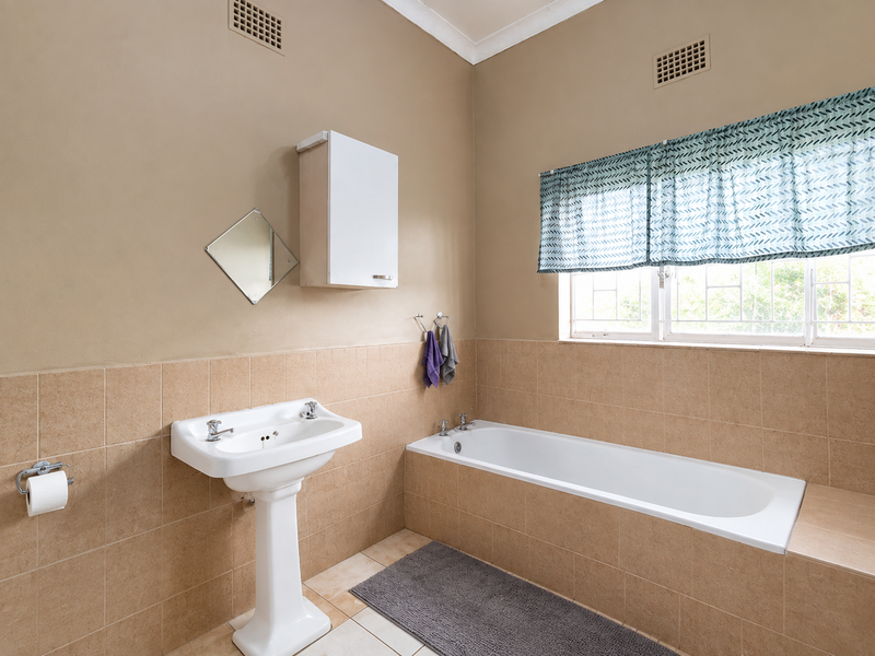 A functional bathroom featuring a pedestal basin, a tiled built-in bathtub, and neutral wall finishes with natural light from the window.