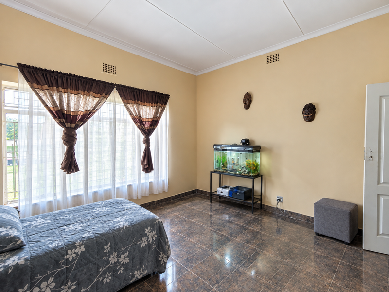 A bedroom featuring tiled flooring, ceiling vents, and large windows with security bars, offering a functional space with neutral wall tones.