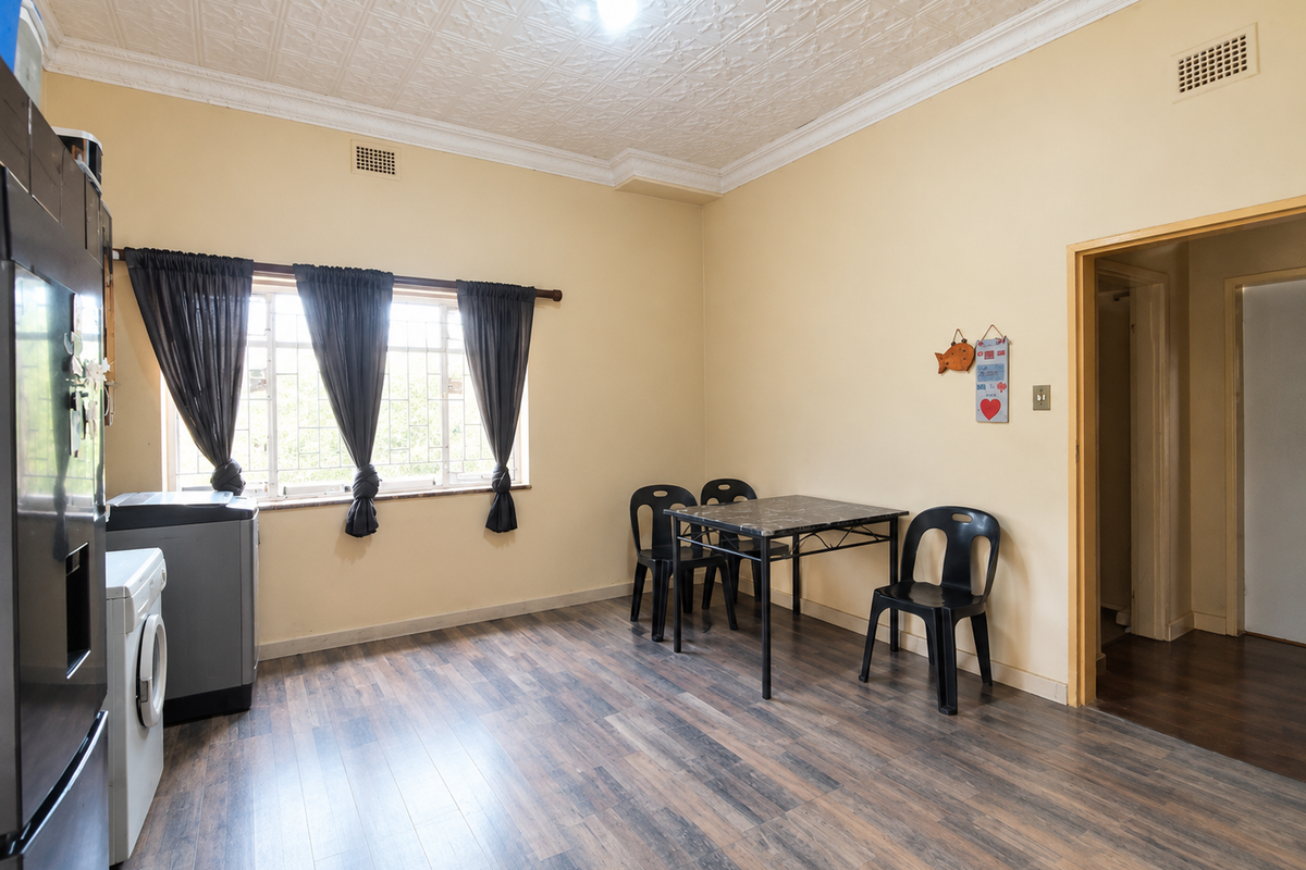 A functional kitchen area featuring laminate flooring, a decorative pressed metal ceiling, and security bars on the windows.