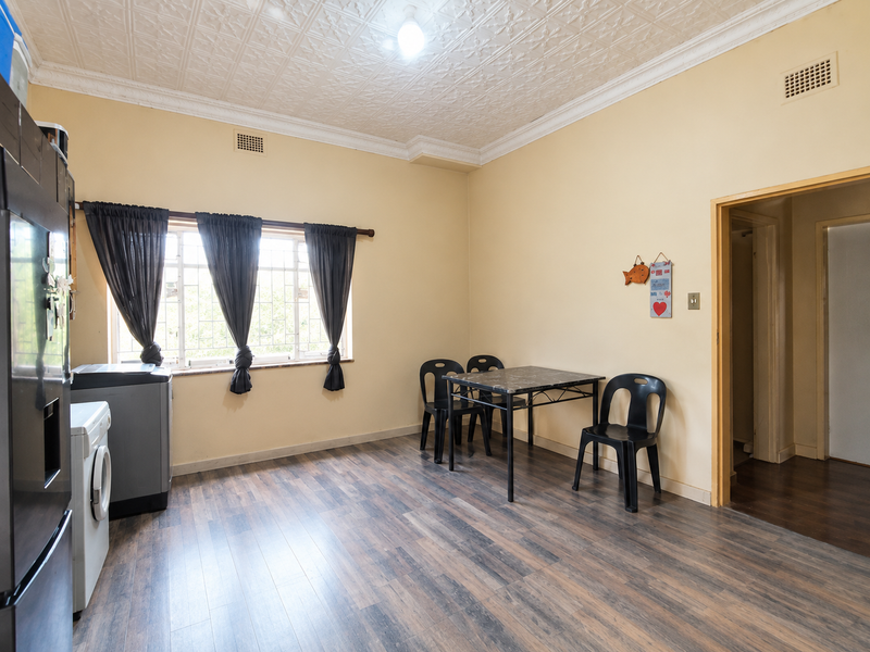 A functional kitchen area featuring laminate flooring, a decorative pressed metal ceiling, and security bars on the windows.