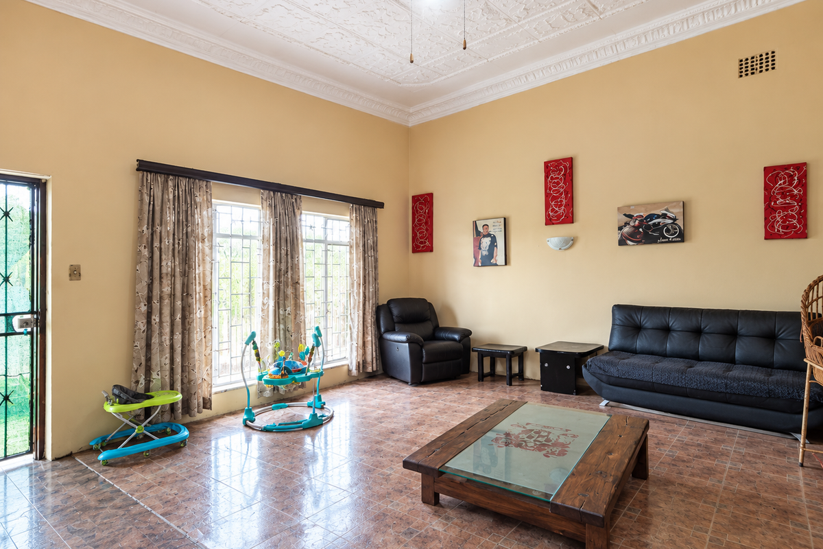 Spacious living room featuring ornate ceiling detailing, tiled flooring, and large windows with security bars, providing a bright and functional living space.