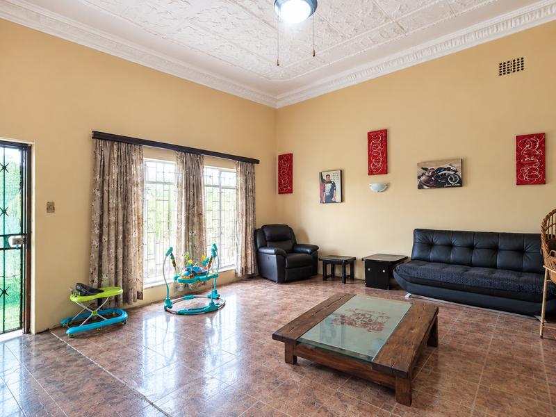 Spacious living room featuring ornate ceiling detailing, tiled flooring, and large windows with security bars, providing a bright and functional living space.