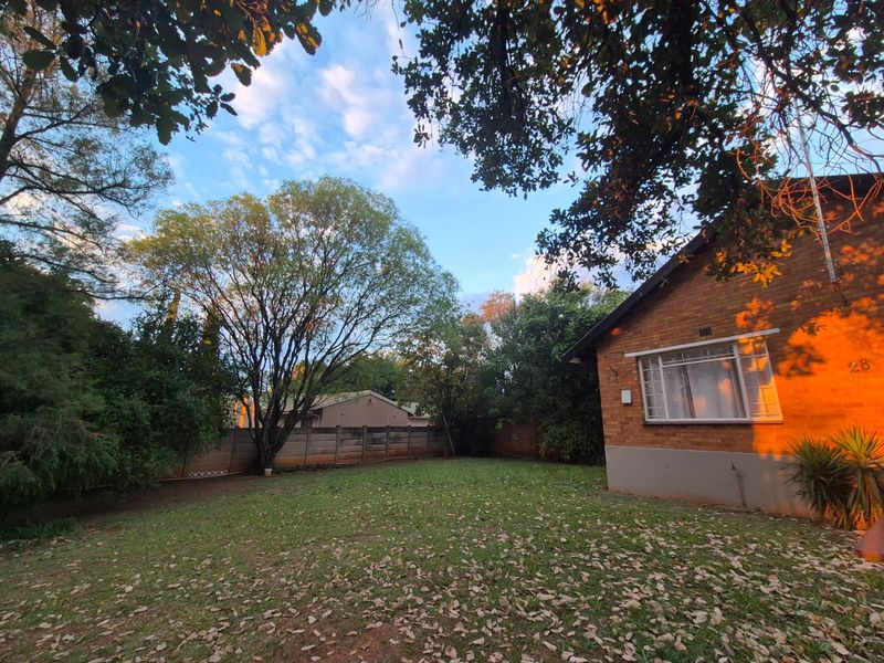 A view of the rear garden featuring a brick exterior wall, established trees, and a precast concrete boundary fence.