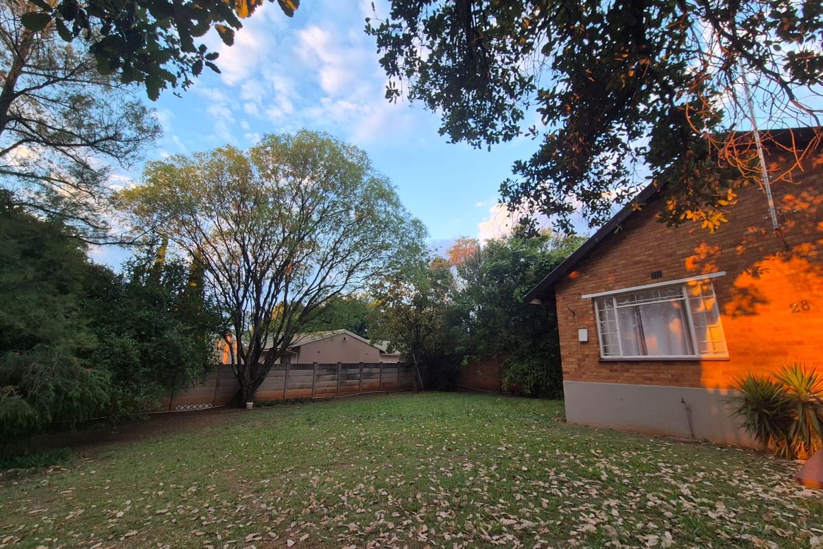 A view of the rear garden featuring a brick exterior wall, established trees, and a precast concrete boundary fence.