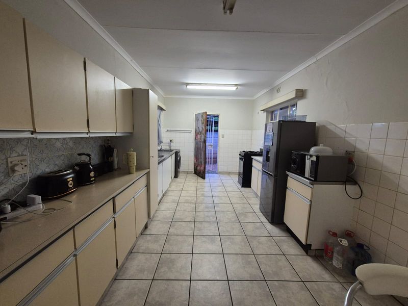 A functional galley-style kitchen featuring tiled flooring, extensive built-in cabinetry, and a tiled splashback, offering a practical layout with direct access to the exterior.